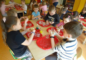Dzieci mieszają składniki na ciastolinę na tackach rozłożonych przed każdym dzieckiem na stole, formują kule.